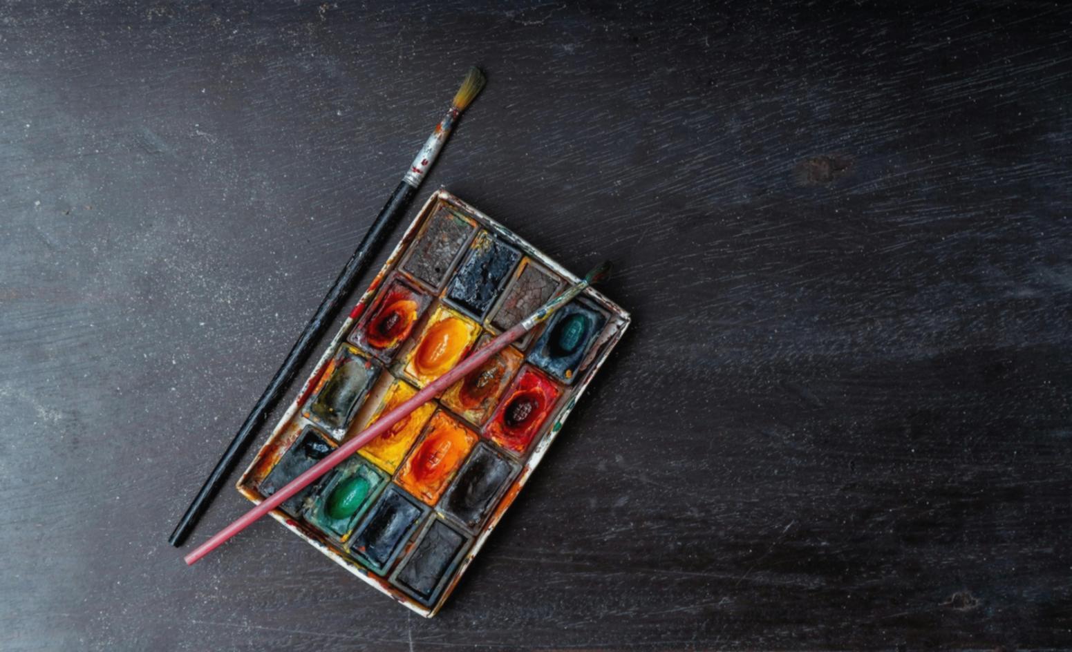 Verschiedene Aquarellfarben und Pinsel auf einem Tisch arrangiert, bereit für einen Malkurs